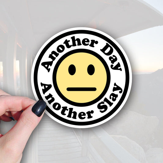 Round sticker with white background, yellow meh face in center. Black font around outer edge that says Another day, another slay.