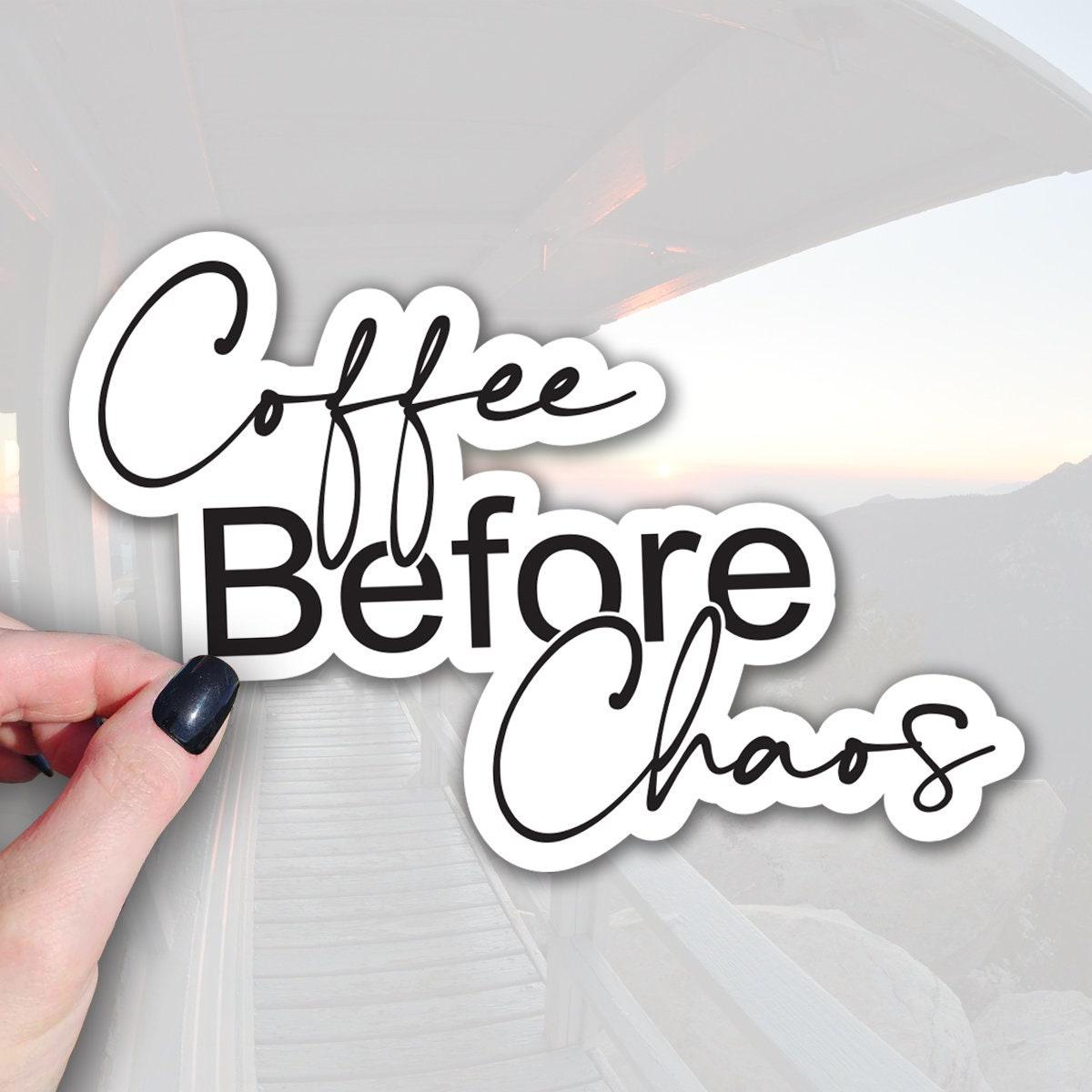 A hand holding a sticker with the text Coffee Before Chaos against a blurred background of a staircase and a sunset.