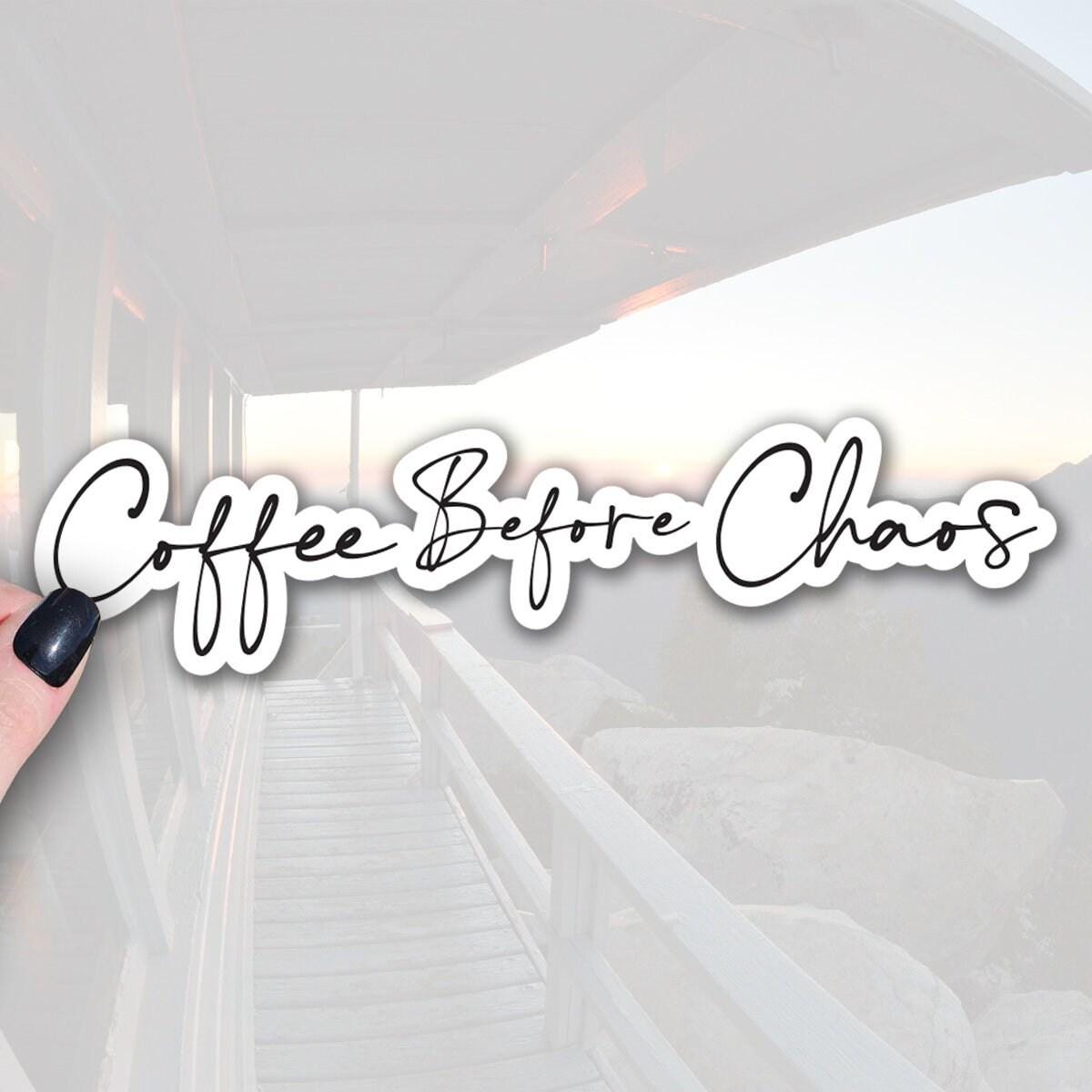 a hand holding a sticker with the text Coffee Before Chaos written on it in black font with white outline.